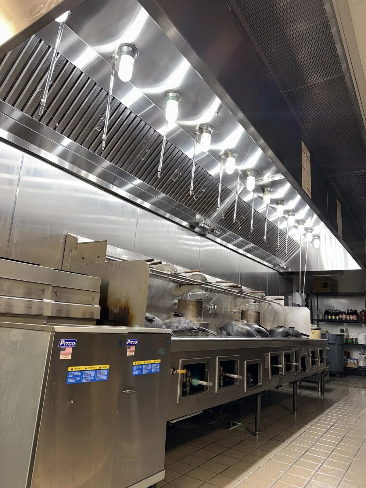 Long stainless steel commercial kitchen hood above a restaurant cooking line